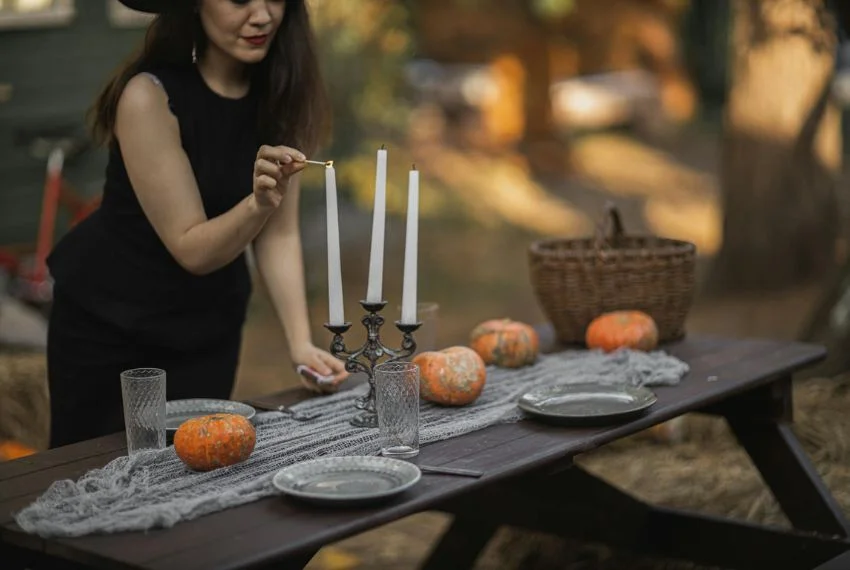 women in black dress lighting candles on table with small pumpkins