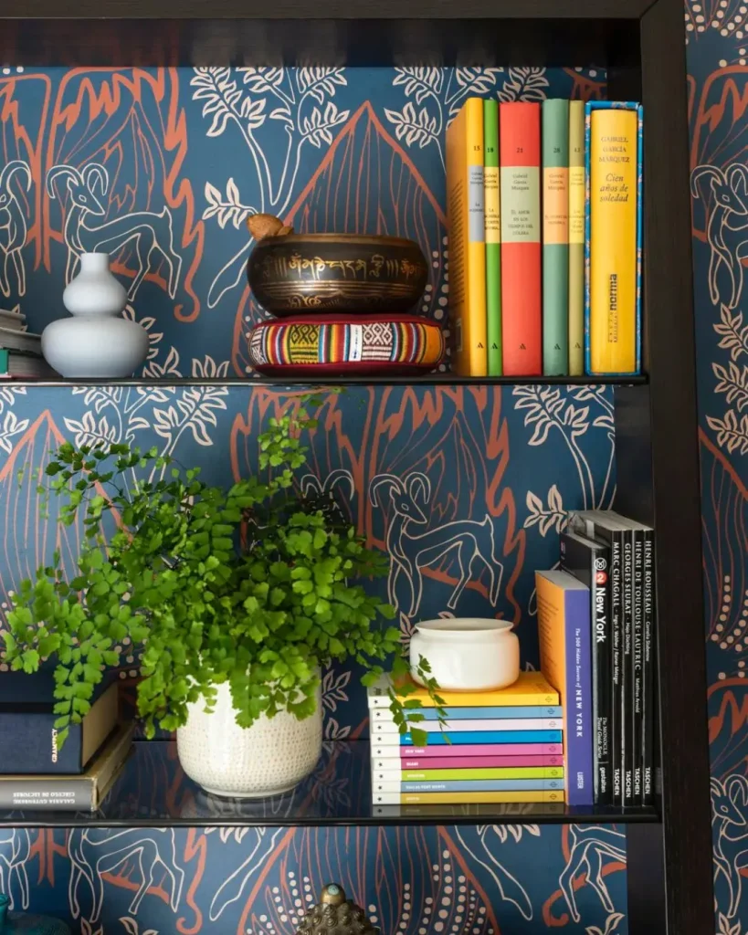 Bookcase with navy floral wallpaper behind colourful books and white ceramics