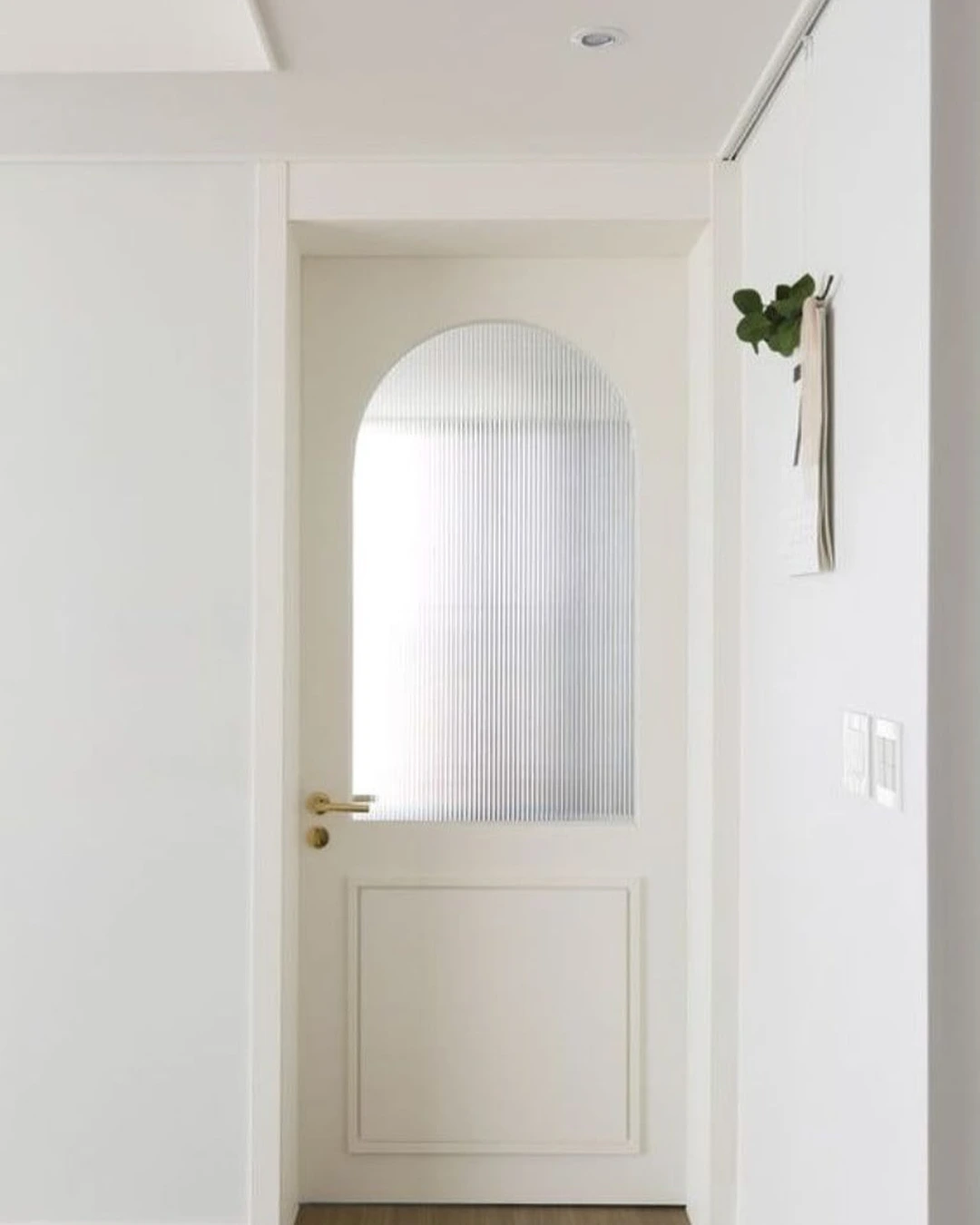 White interior door with a large arched frosted-glass panel and gold lever handle