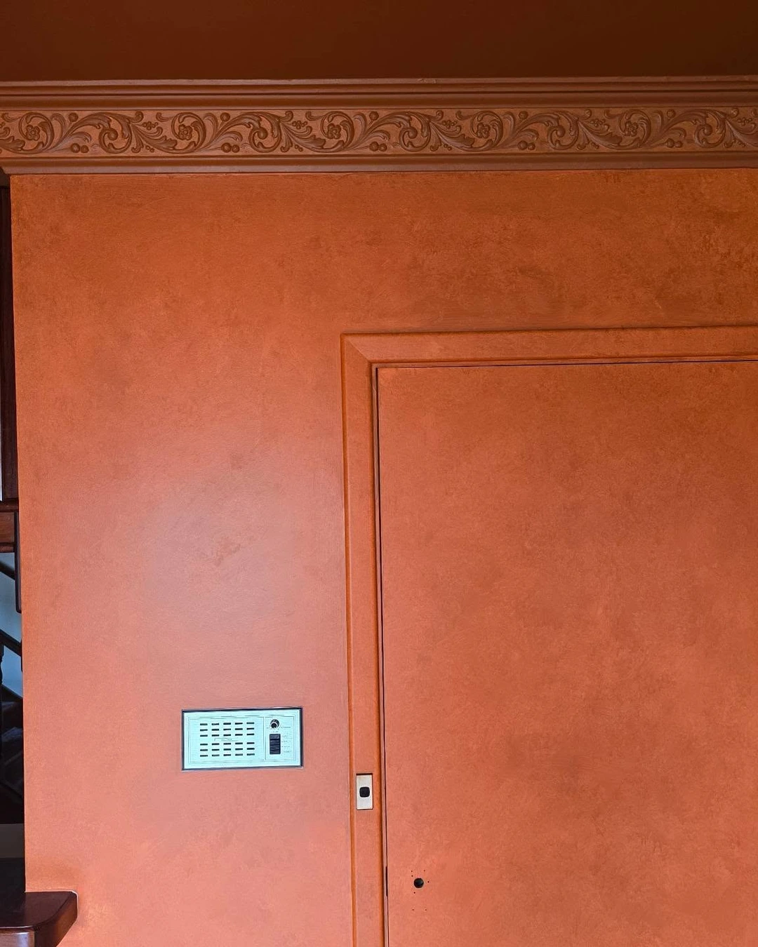 Flush terracotta door painted the same warm rust color as the wall and crown molding