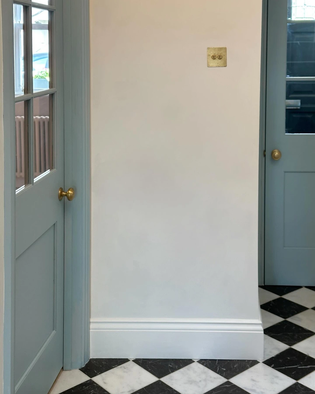 Two soft blue-gray paneled doors with brass knobs in a hallway with diamond marble floor