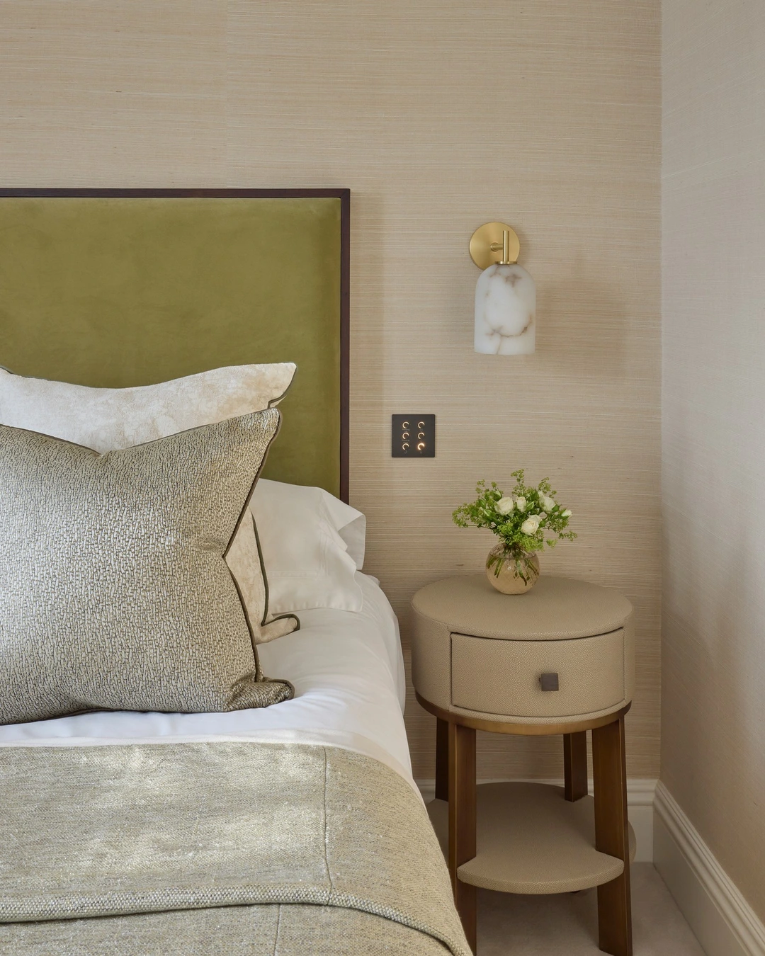 Bedroom with warm beige grasscloth walls, olive headboard and marble sconce
