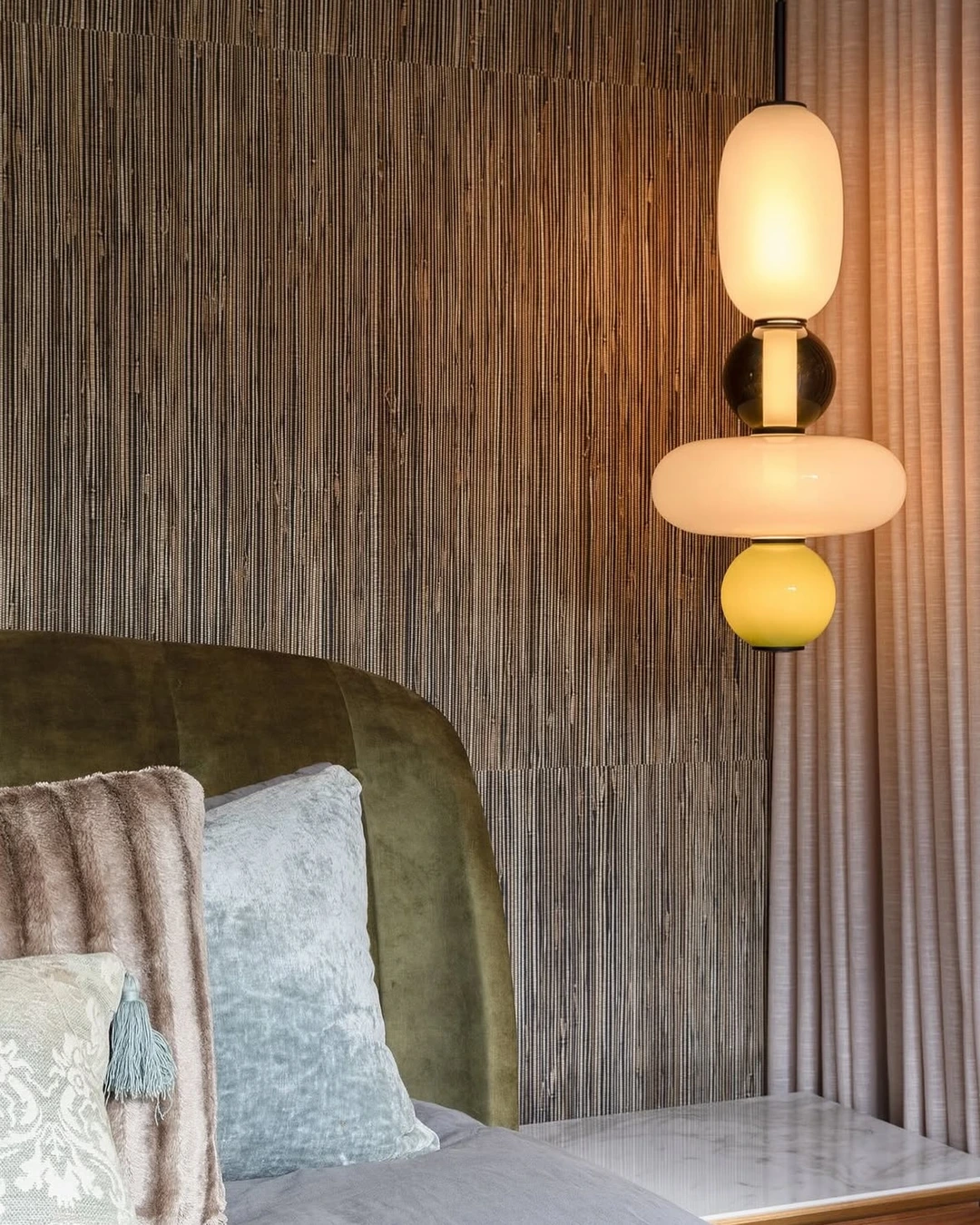 Vertically hung grasscloth wall behind an olive-green velvet headboard