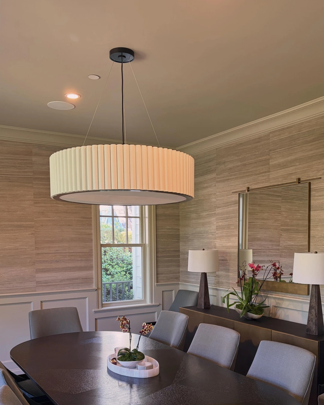 Dining room with grasscloth walls above white wainscoting, round dark table and drum pendant