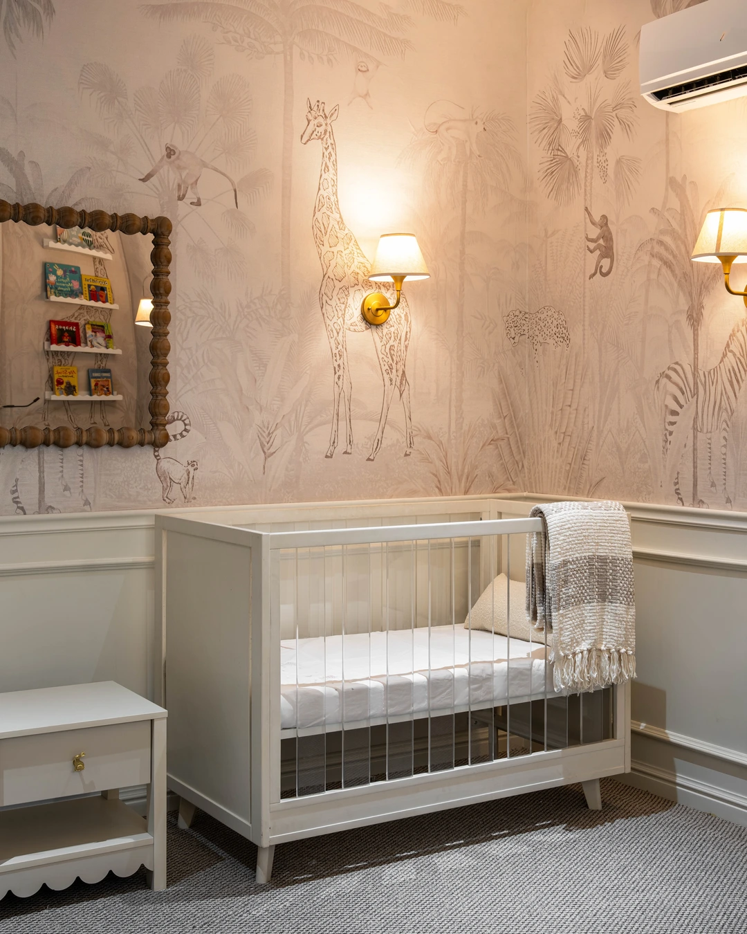 Nursery with jungle mural grasscloth wall, white crib and brass sconces