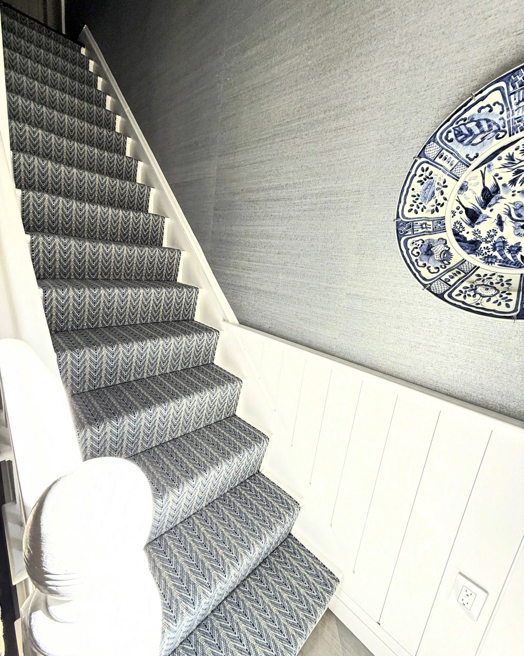 Staircase with chevron runner beside a gray grasscloth wall and decorative plate