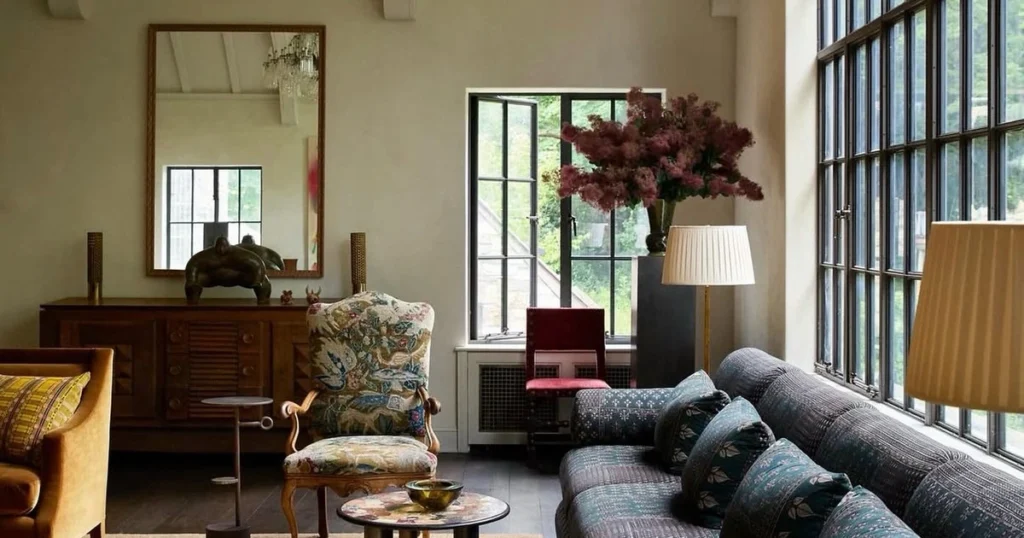 Spacious high-ceiling living room with limewash walls, tall black-framed windows, long dark-blue sofa and floral armchair