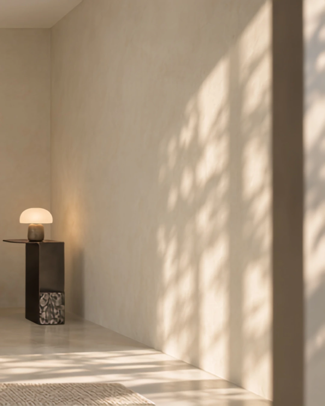 Minimalist sunlit room corner with subtle suede-textured beige walls and a mushroom lamp on a side table