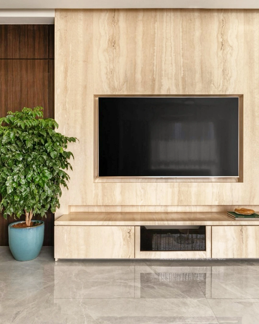Light travertine feature wall with a recessed television, matching console and dark wood paneling