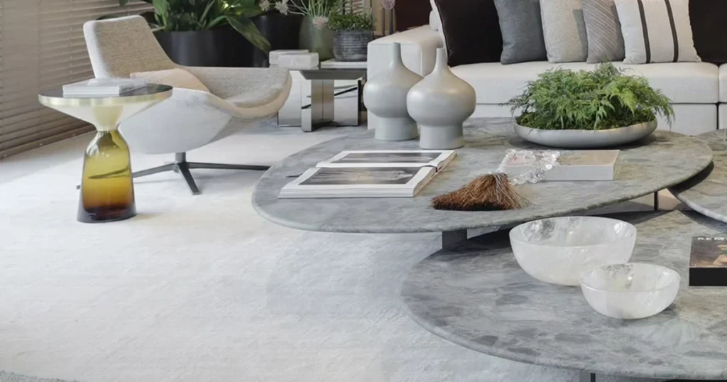 Bright living room with a white sectional sofa, a swivel chair, and round marble coffee tables with books, vases, and a plant bowl