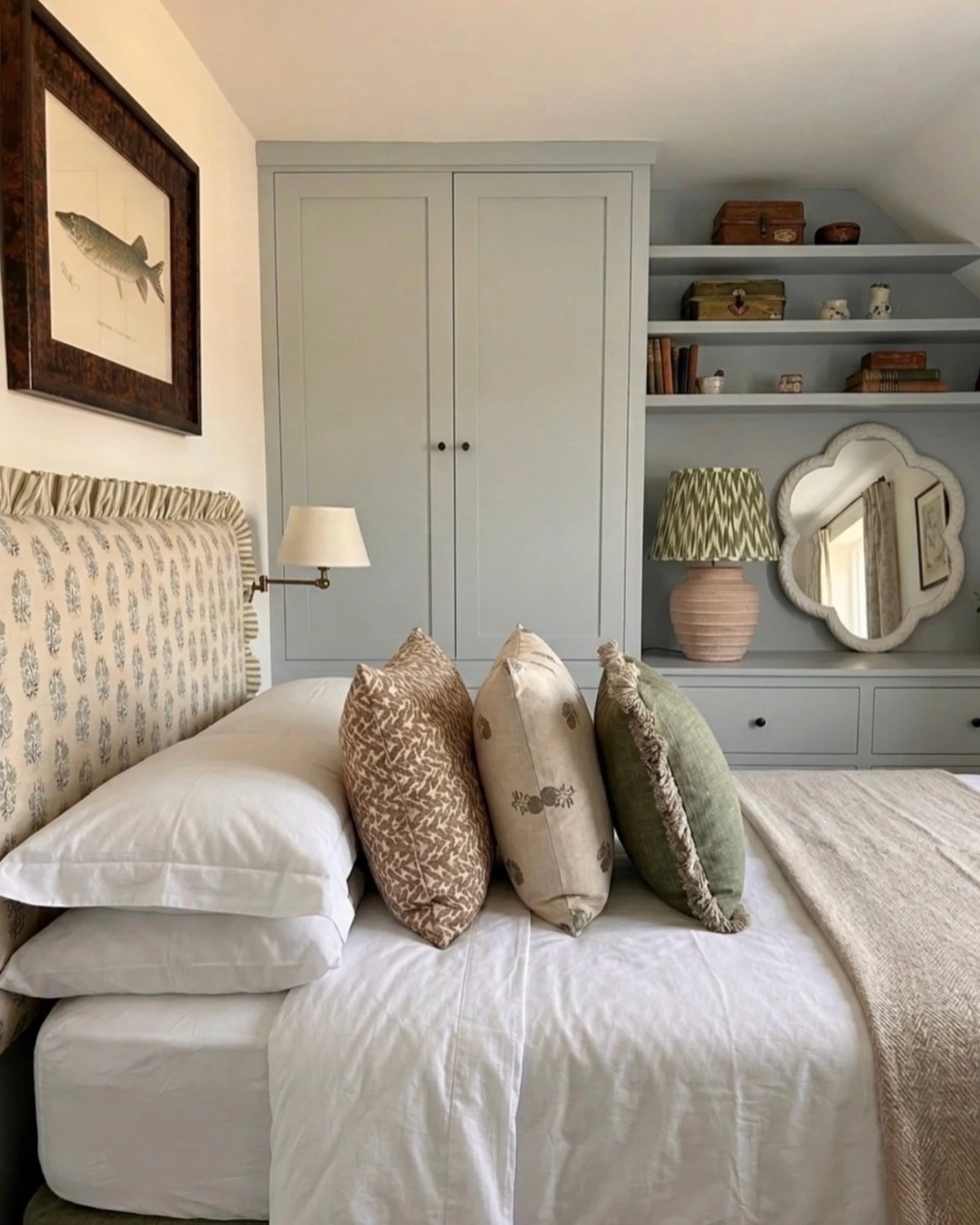 Neatly made bed with white linens, stacked sleeping pillows, and three decorative cushions against a leaf-print headboard