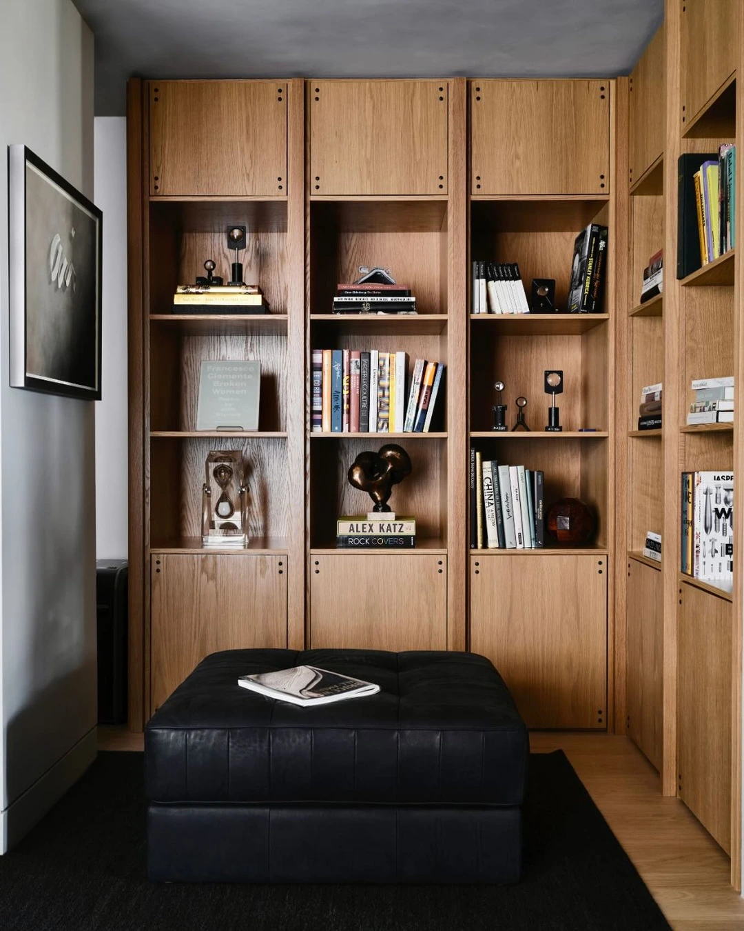 Light wood built-in shelves with books arranged upright and in horizontal stacks, an hourglass, and small sculptures