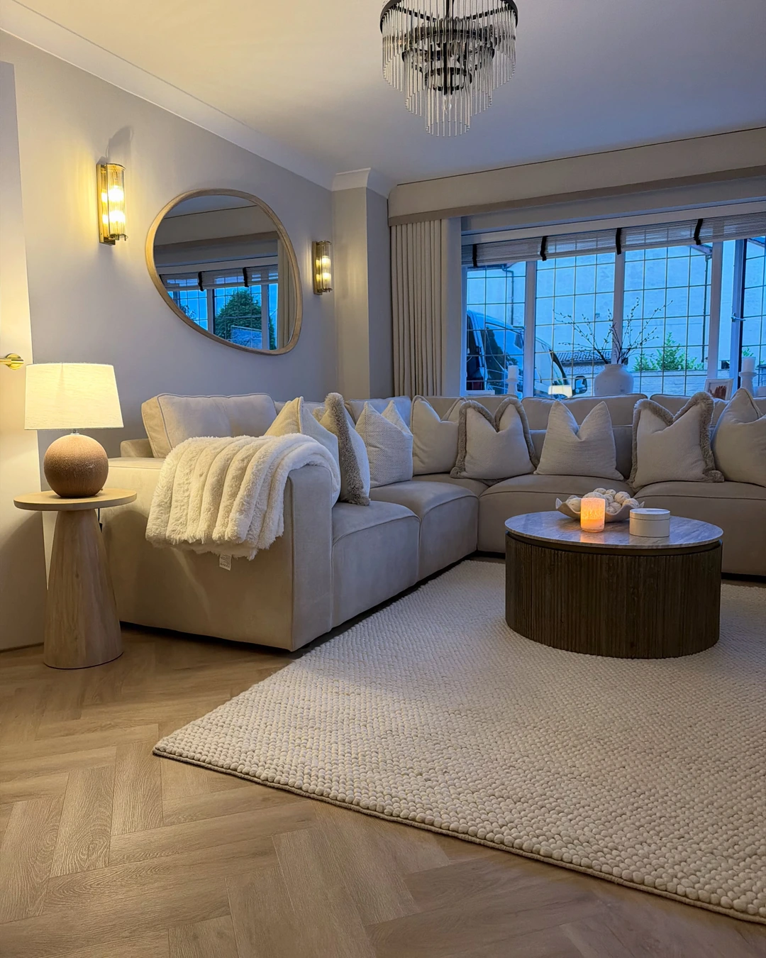Light grey sectional sofa with neutral cushions and a cream fluffy throw draped over one arm, beside a round coffee table with a lit candle