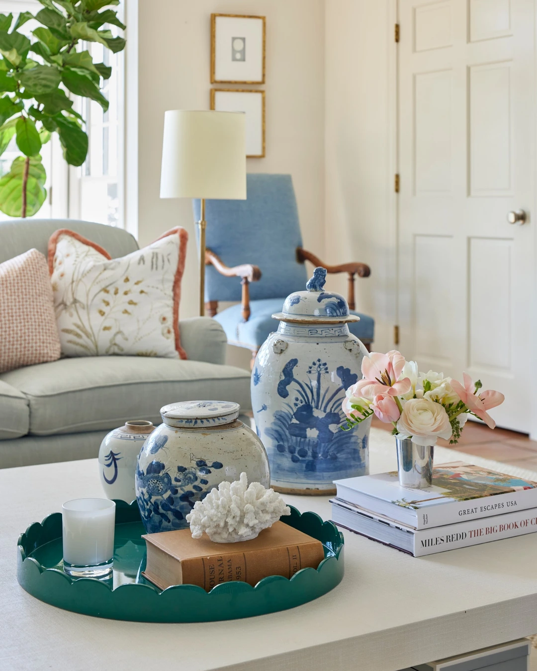Green scalloped tray on a coffee table holding a candle, a book, and a white coral decoration beside blue-and-white ginger jars