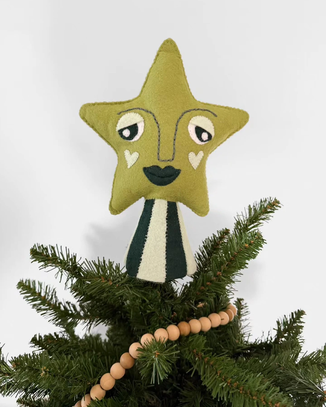Olive-green felt star with an embroidered face on a striped cone base at the top of a Christmas tree