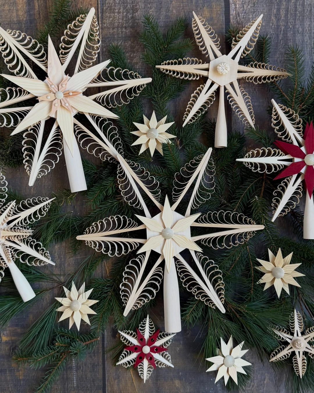 Collection of light-wood carved star tree toppers arranged on pine branches, two with red centers