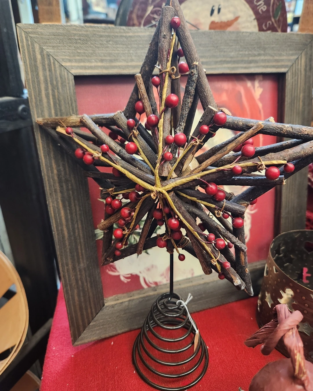 Twig star tree topper with red berries on a black metal coil base, photographed off the tree