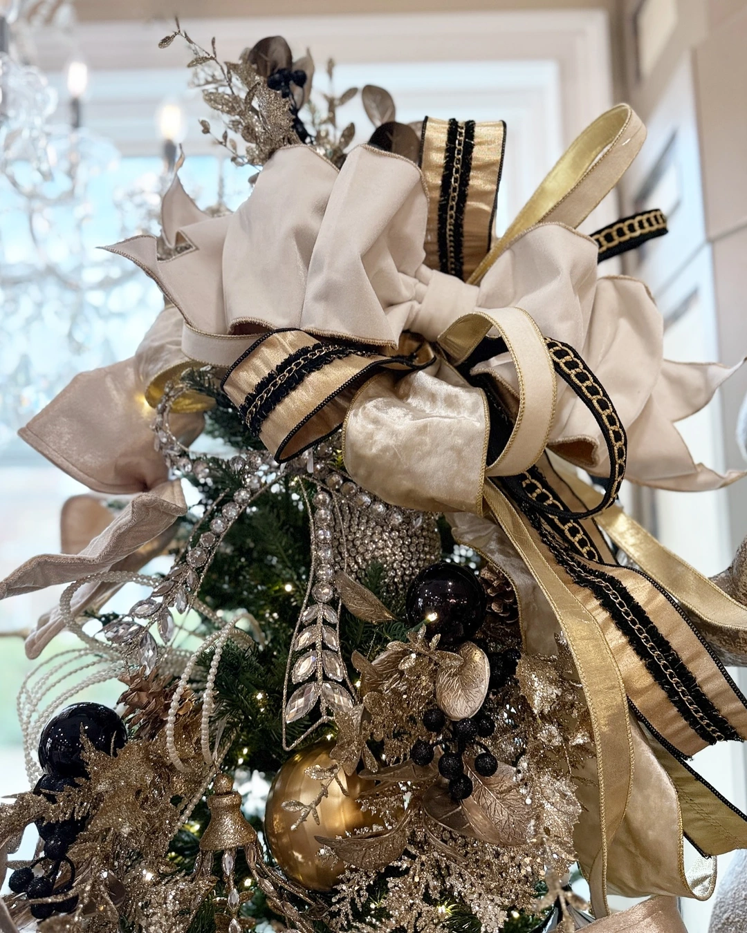 Cream velvet bow layered with gold satin ribbon trimmed in black on top of a decorated Christmas tree