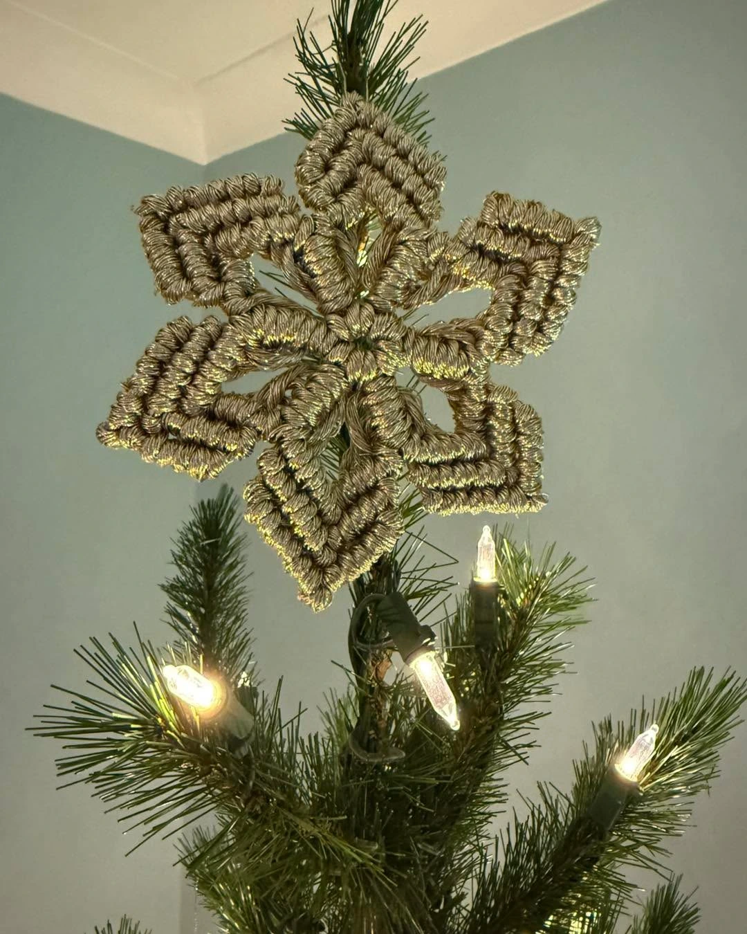 Gold macrame snowflake tree topper crowning a lit Christmas tree