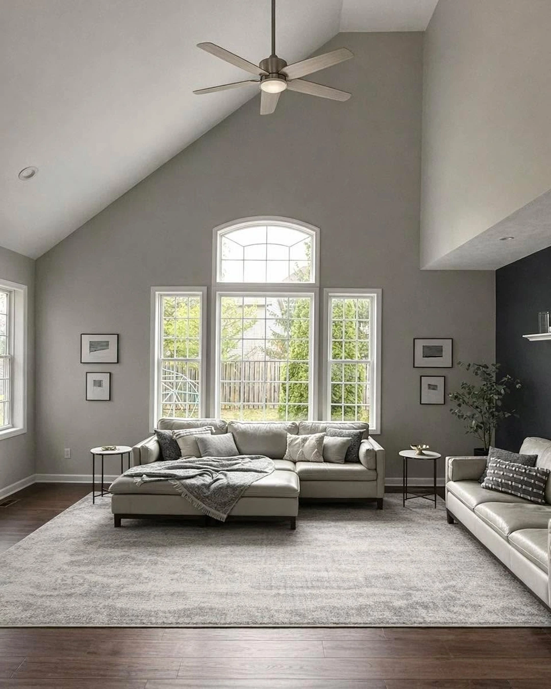 Living room with light gray walls, tall windows, light leather sofas, and a dark accent wall on the right.