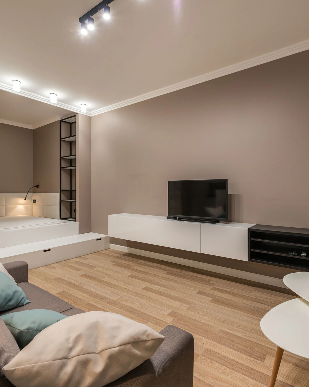 Living room with warm beige-taupe walls, a wall-mounted TV, white storage units, and a curtained sleeping nook.