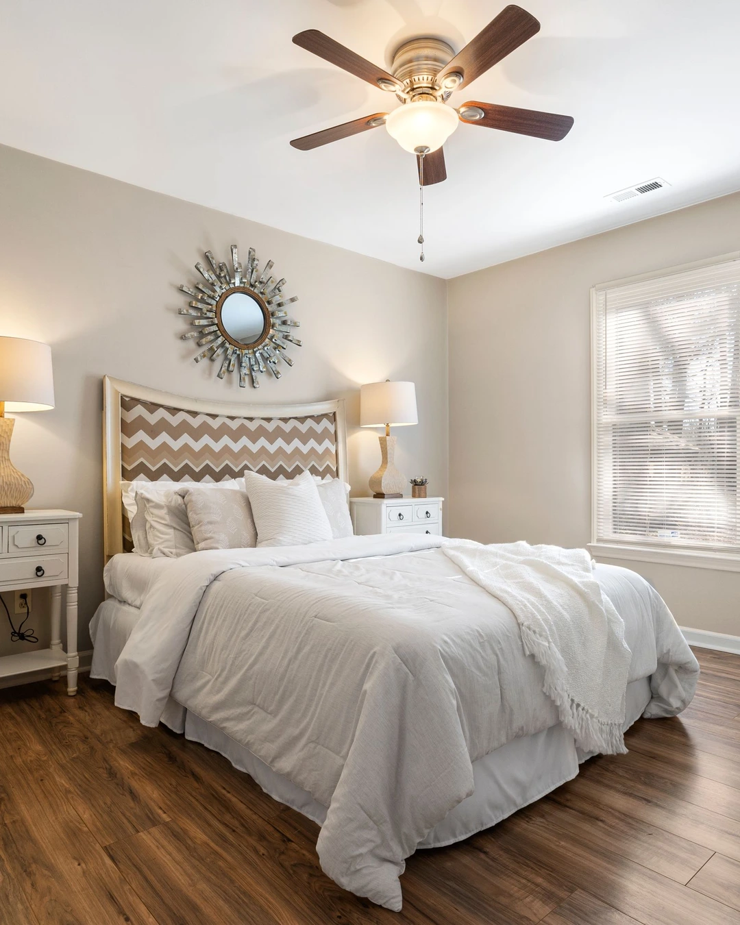 Bedroom with warm creamy walls, white bedding, a chevron headboard, and a sunburst mirror.