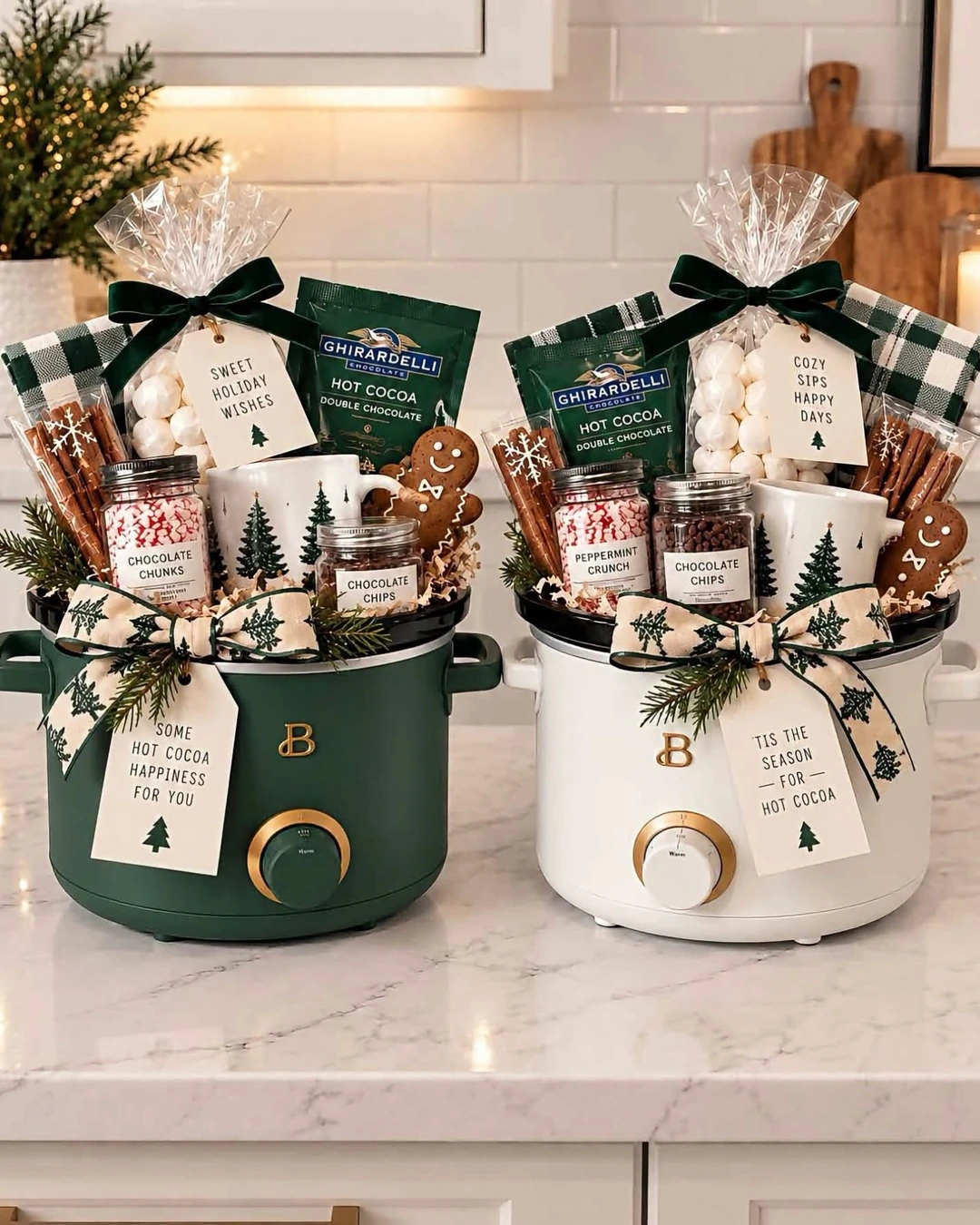 Two mini slow cookers, green and white, filled with hot cocoa packets, marshmallows, jars, tree-print mugs, and gingerbread cookies.