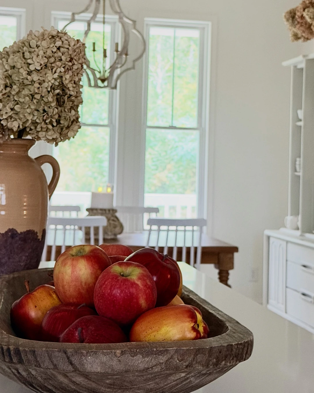 Rustic wooden dough bowl filled with red and yellow apples on a white kitchen island.