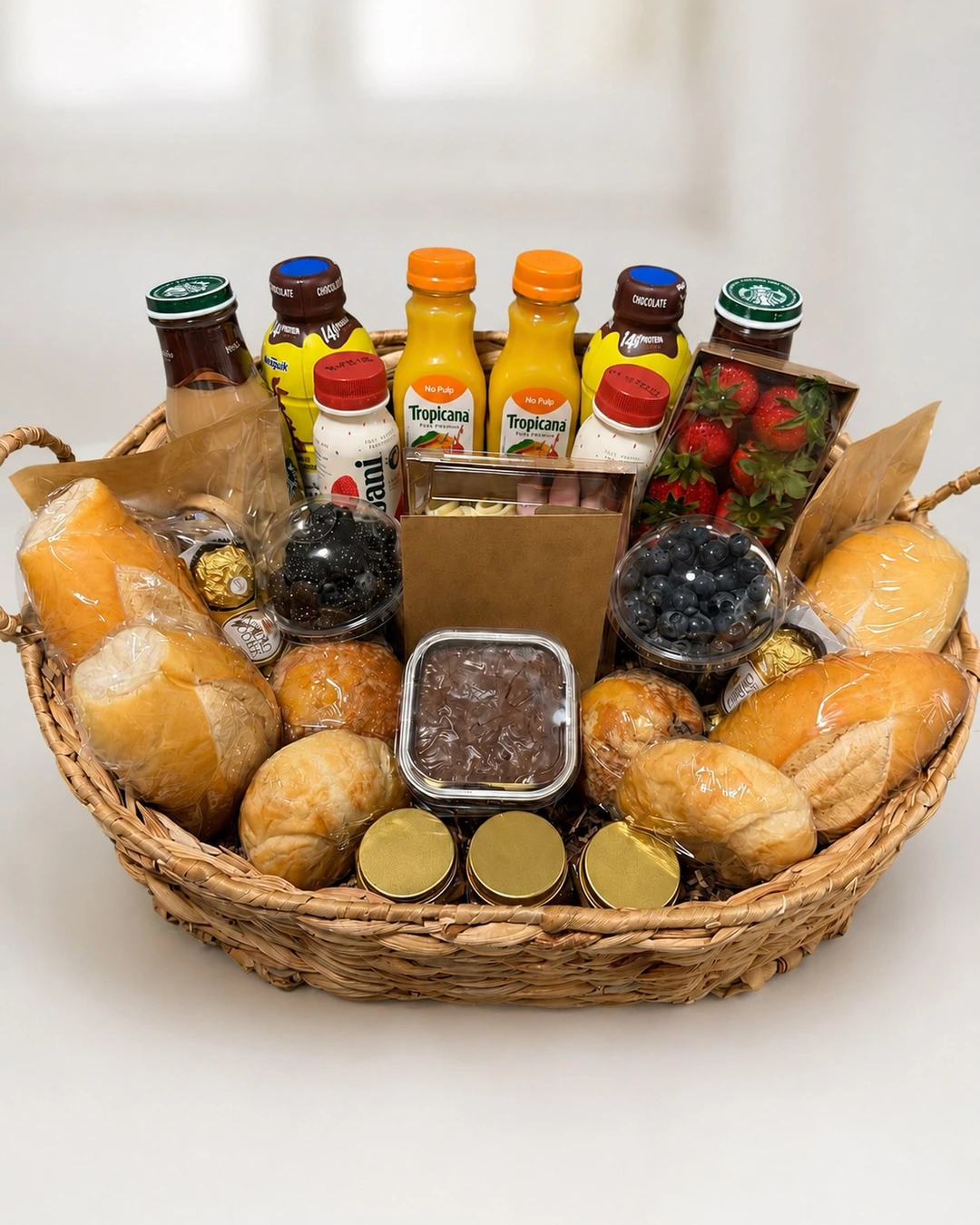 Wide wicker basket with wrapped rolls and pastries, berries, orange juice, chocolate milk, bottled coffee, yogurt drinks, and chocolates.