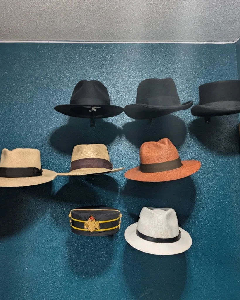 Hat collection on a dark teal wall with black fedoras, straw hats, a black cap with gold trim, and a white fedora