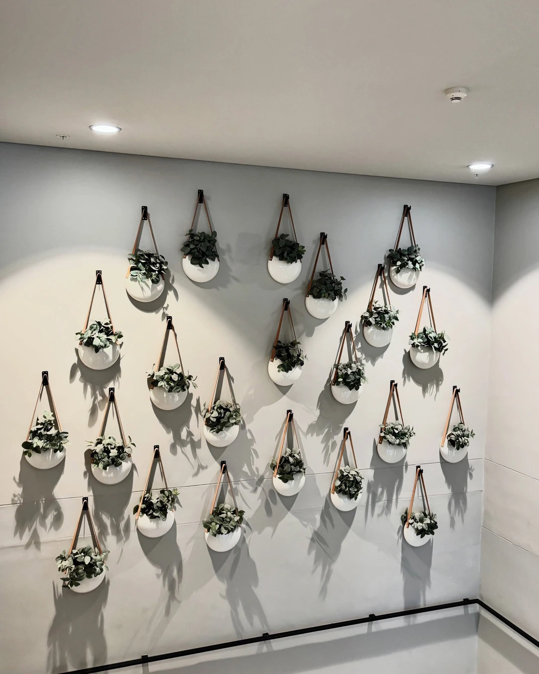 White spherical hanging planters with artificial greenery arranged in an asymmetrical grid on a light gray stairwell wall
