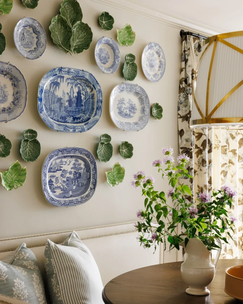 Blue-and-white porcelain plates and green cabbage-shaped dishes arranged on a cream dining nook wall above a banquette