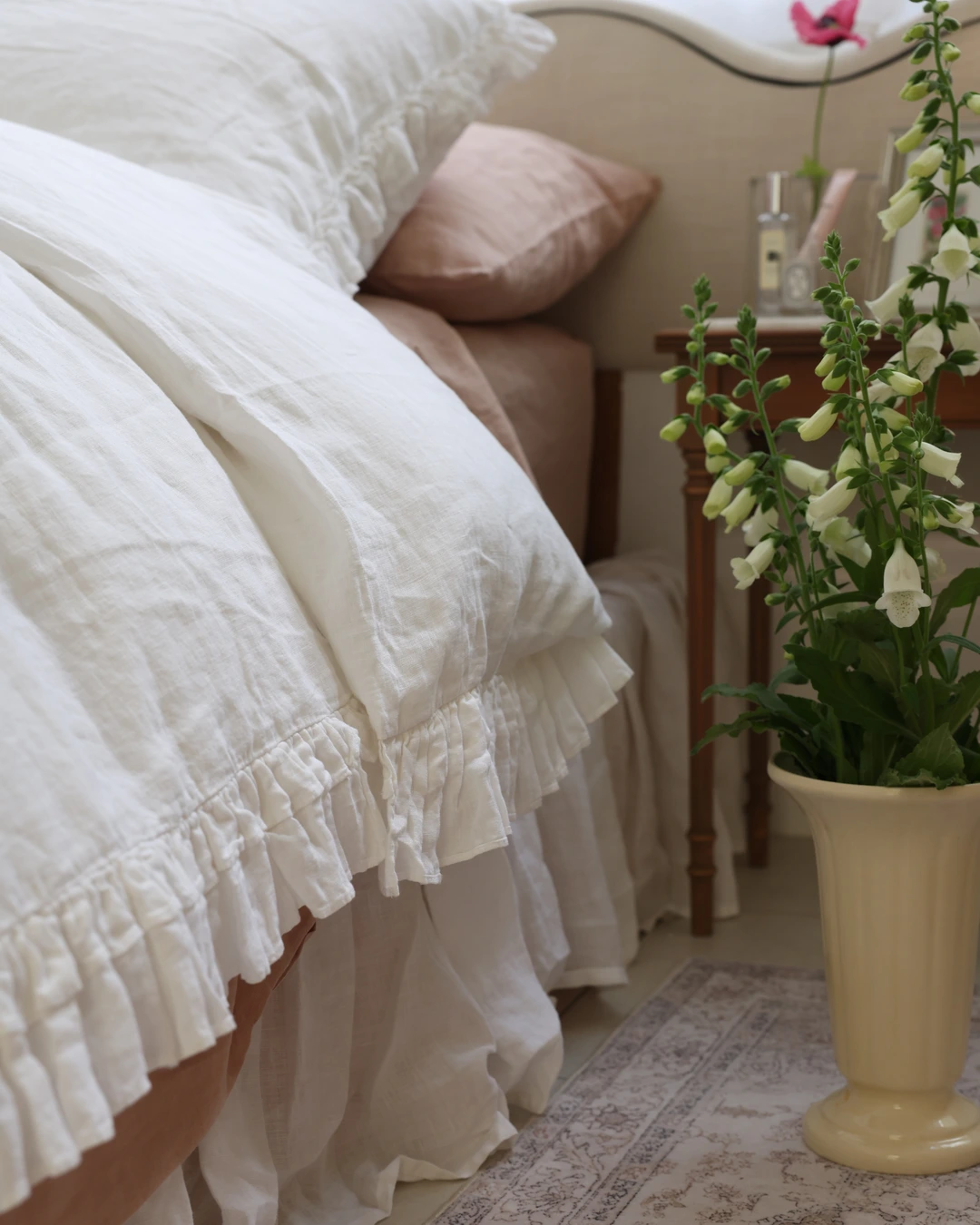 White linen bedding with a ruffle hem and ruffled pillow edges beside a terracotta-pink accent pillow