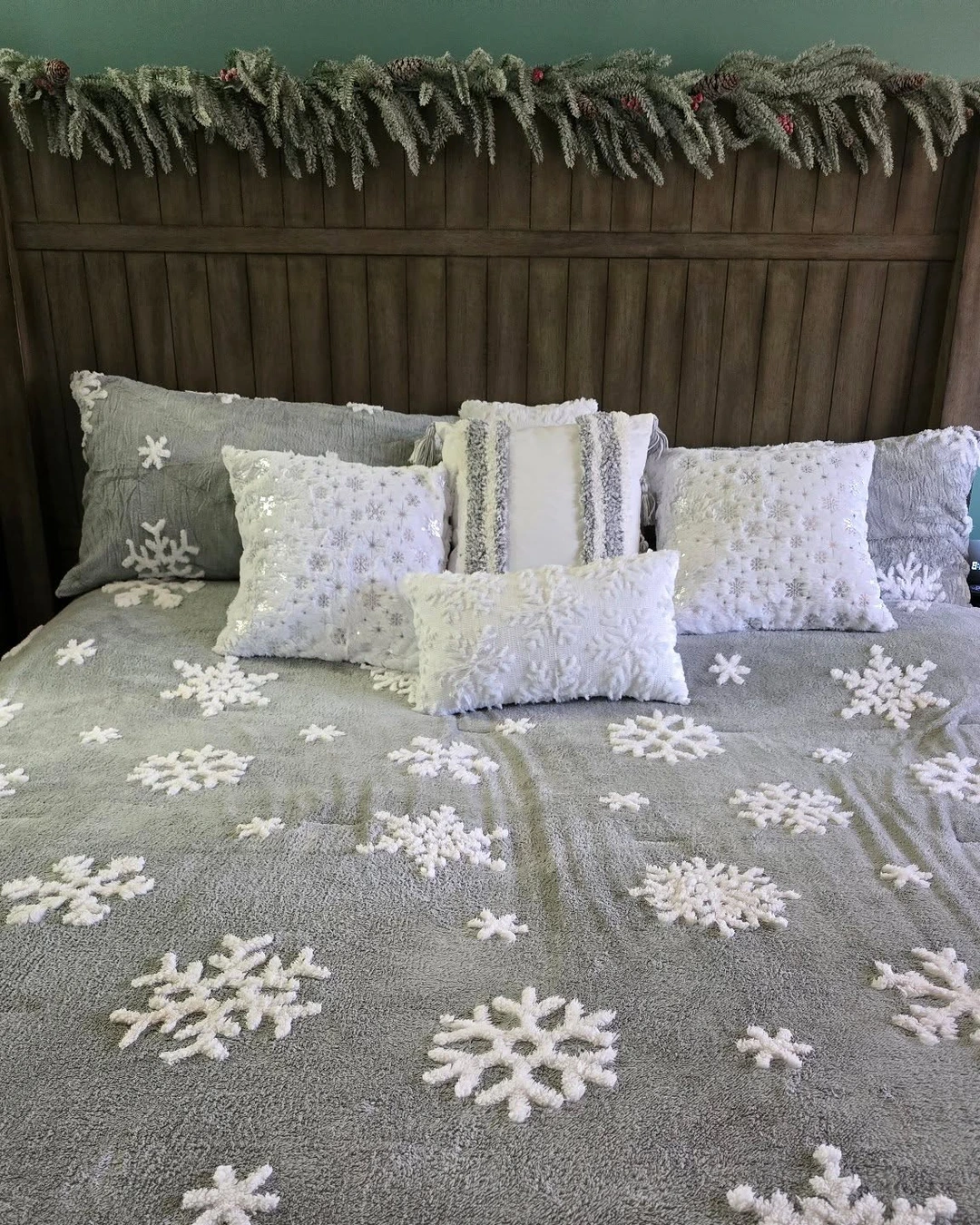 Bed with grey comforter with white snowflake appliques, white and silver pillows, and frosted garland above the headboard.