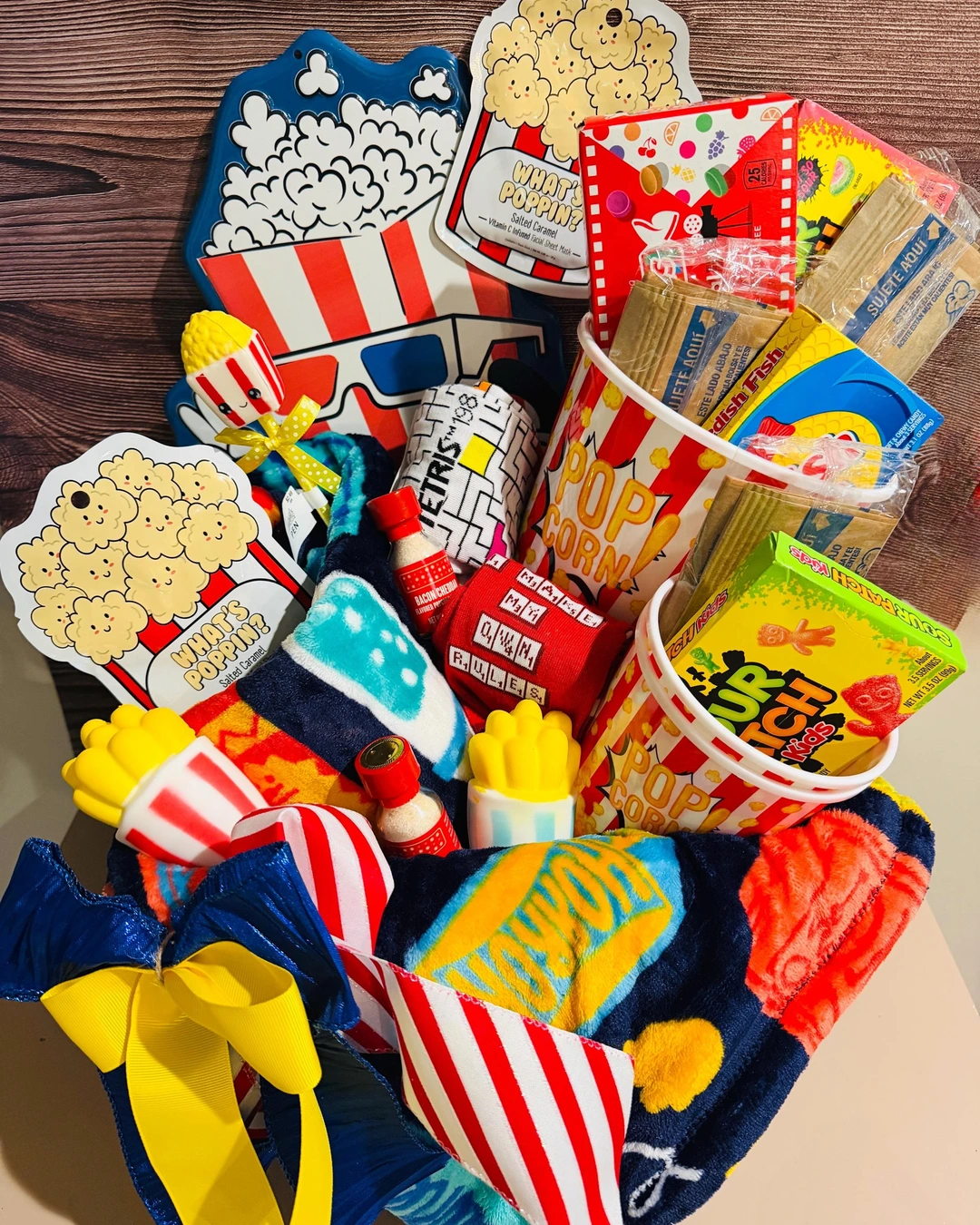 Popcorn buckets filled with candy, popcorn seasoning, socks, face masks, and toys, with a plush blanket and popcorn wall decor.
