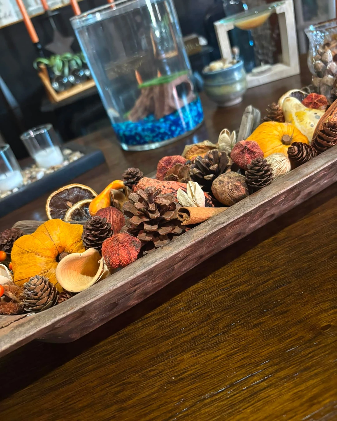 Close-up of a long dough bowl with pinecones, dried orange slices, cinnamon sticks, seed pods, and small pumpkins and gourds.