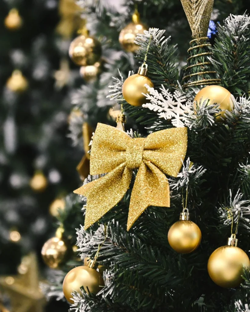 Frosted Christmas tree branches with gold baubles, a large gold glitter bow, and white snowflake ornaments.