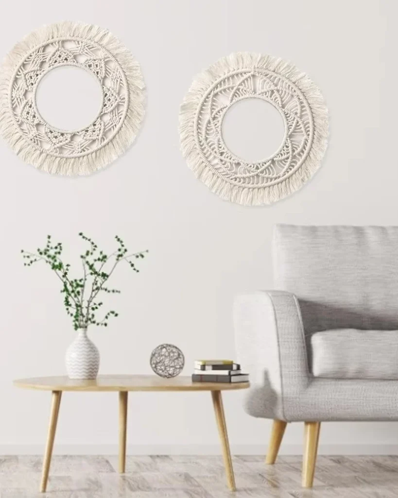 Two circular cream woven wall hangings with fringe above a light wood coffee table and gray armchair