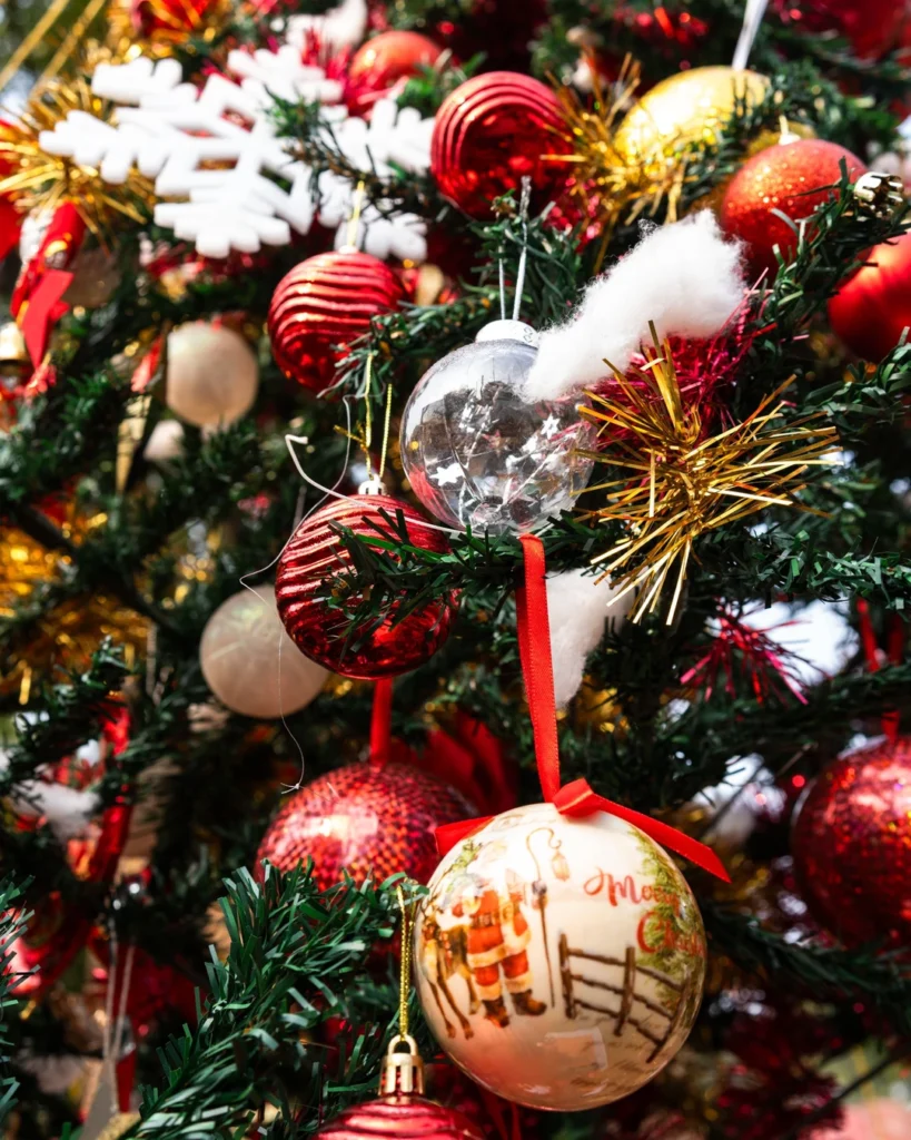 Dense Christmas tree with red and gold baubles, gold tinsel, white snowflakes, and a cream Santa bauble.
