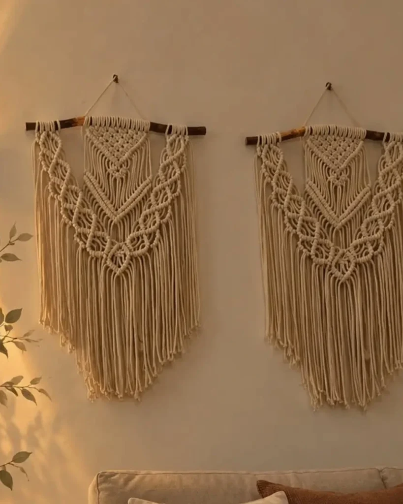 Two matching cream macrame wall hangings on wooden dowels above a sofa