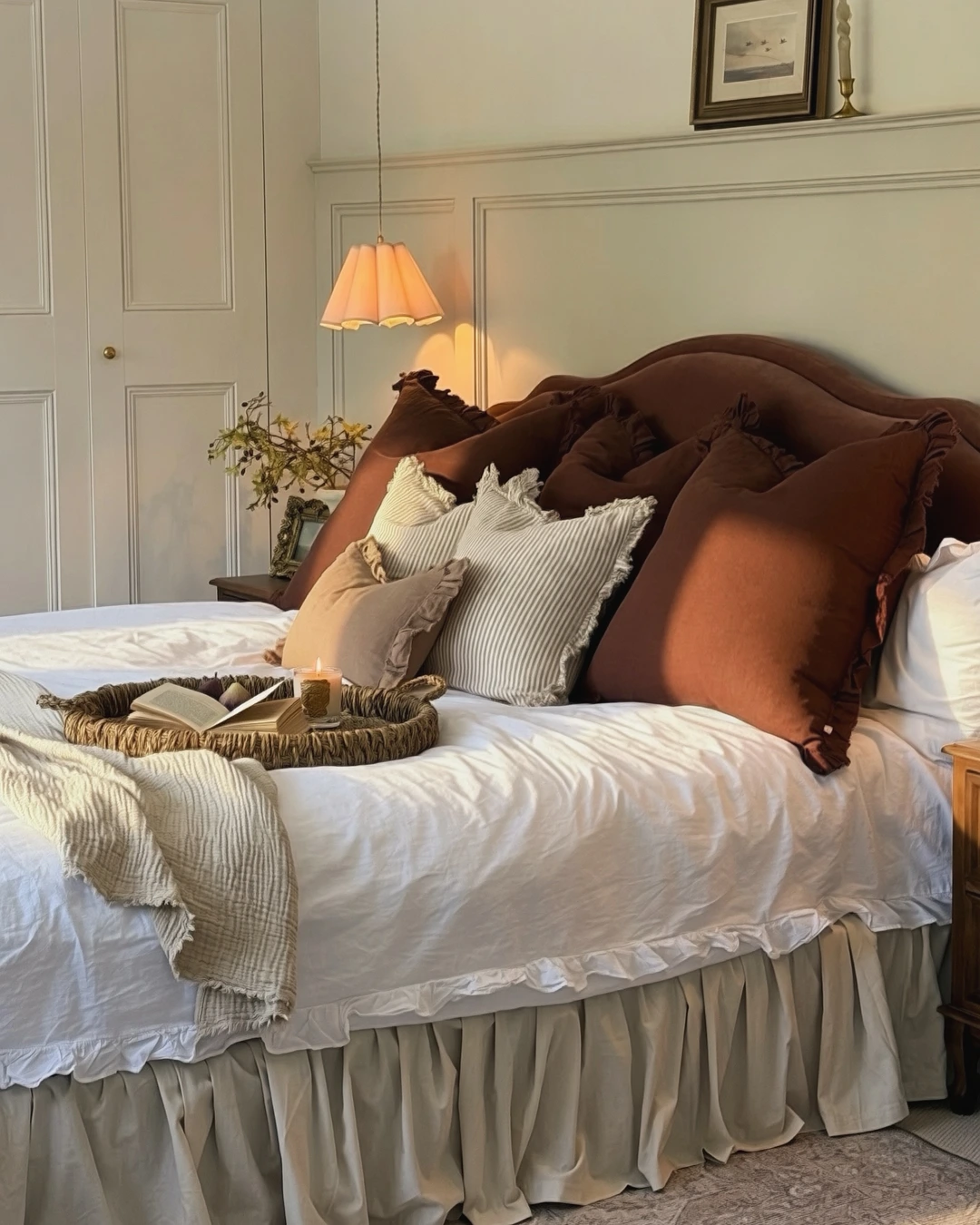 Bed in white linens with a gathered ruffle bed skirt and brown and striped throw pillows