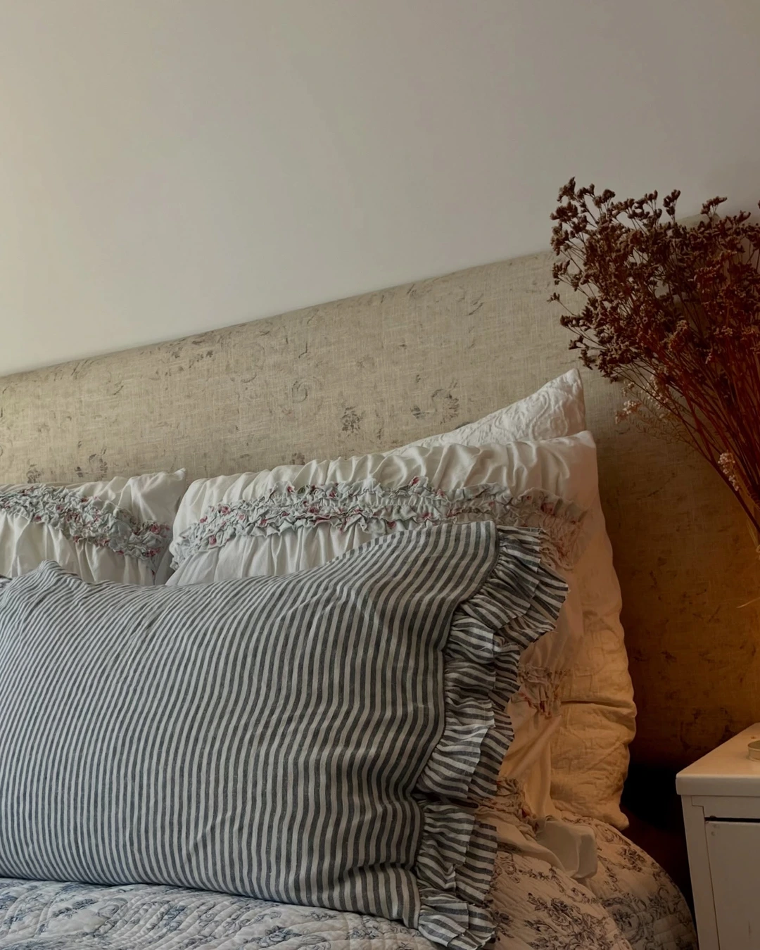 Striped ruffle lumbar pillows in front of white floral-trimmed pillows on a blue toile quilt