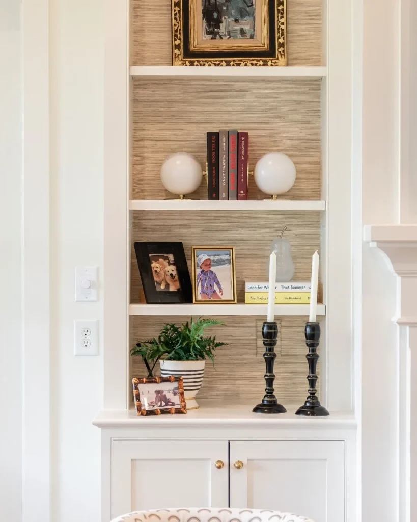 white bookcase lined with oatmeal woven grasscloth-textured wallpaper, rattan baskets